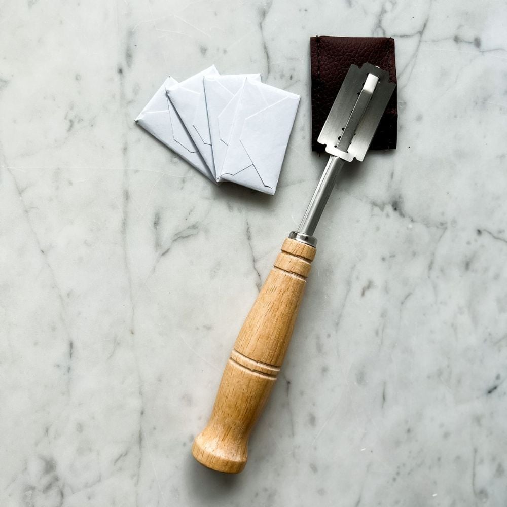 bread lame with a wood handle with 3 blade replacements on marble