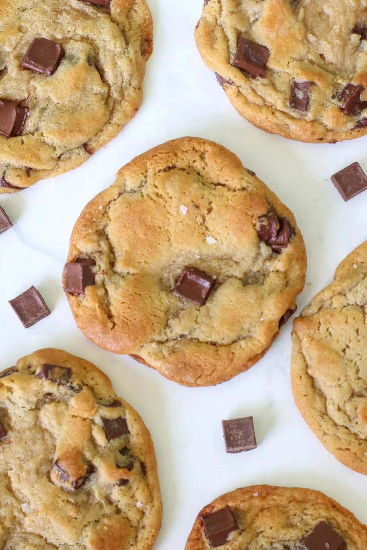 several sourdough chocolate chip cookies on a white board with chocolate chunks.