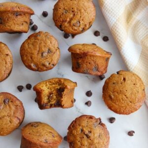 Sourdough pumpkin muffins with chocolate chips scattered around next to a brown and white cloth napkin.