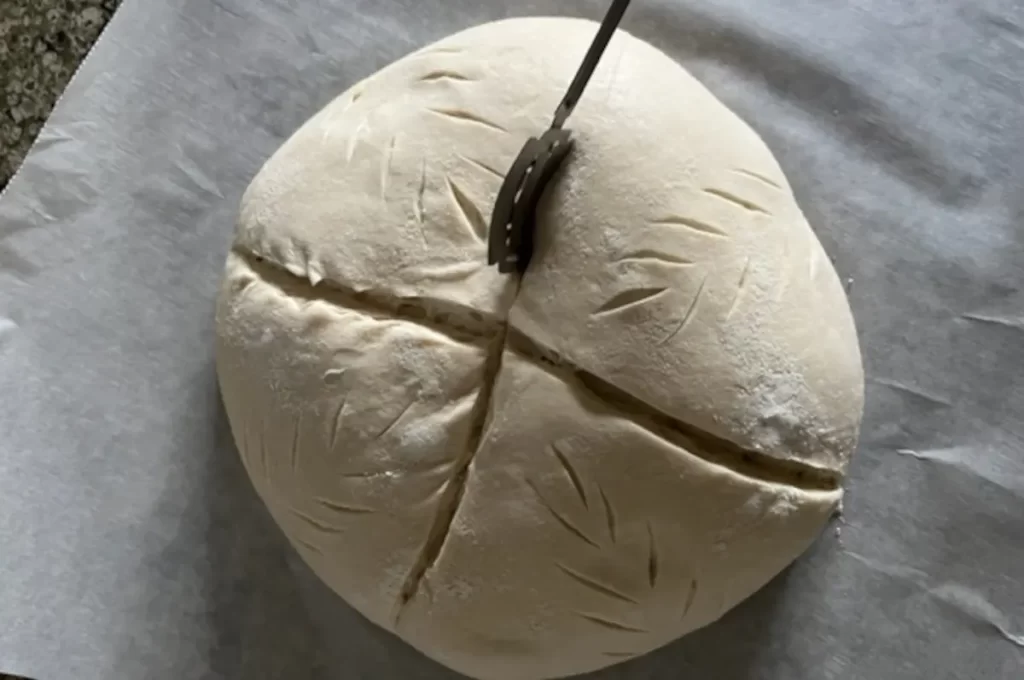 a bread lame scoring a round loaf of sourdough bread