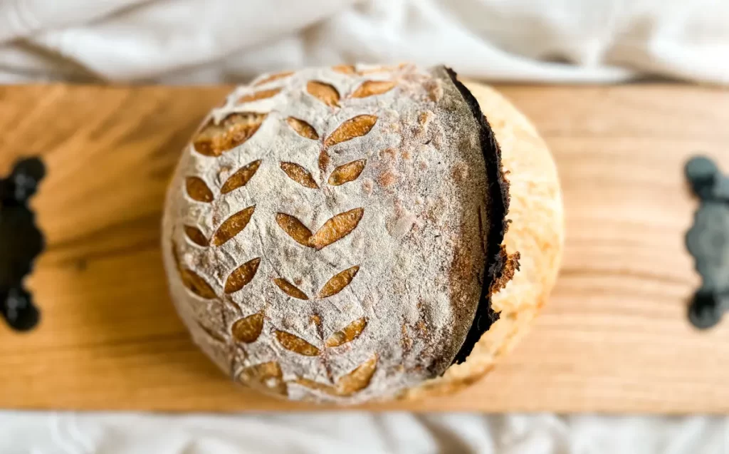artisan sourdough bread boule with 2 rows of wheat stalks and an ear on top of a wood board