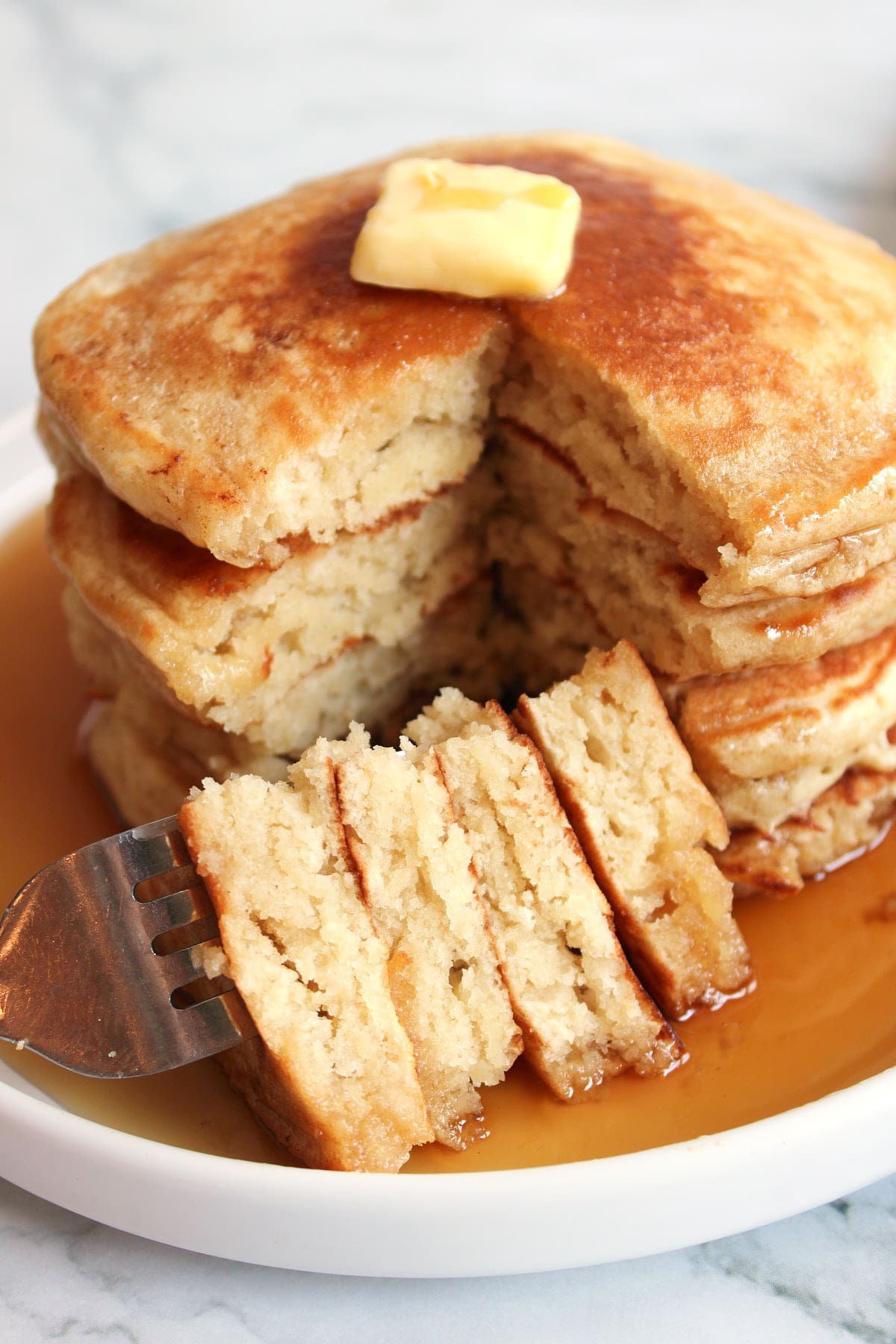 4 Sourdough Discard Pancakes stacked on top of each other with a fork holding a slice of pancake.