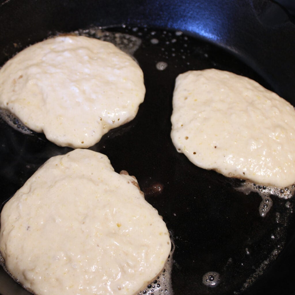 Sourdough discard pancakes cooking in a cast iron skillet.