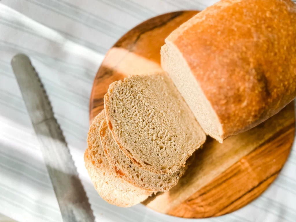 sliced sourdough sandwich bread on a round wooden board with a bread knife 