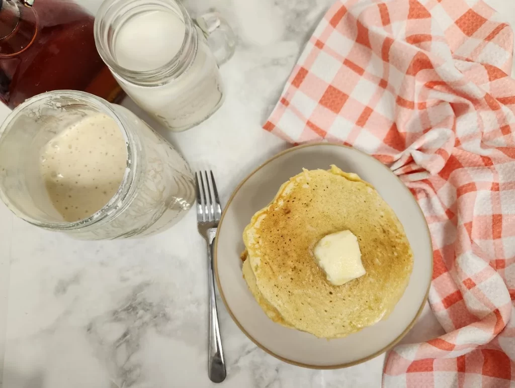 sourdough pancakes on a plate with butter on top next to a glass of milk, sourdough discard and syrup