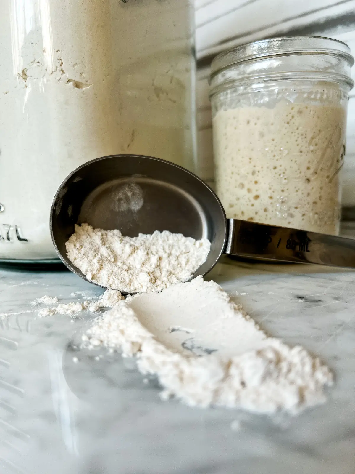 sourdough starter and flour with a cup of flour spilled out in the front