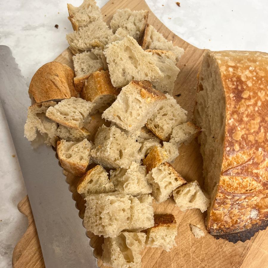 Bread sliced into cubes on a cutting board with a knife