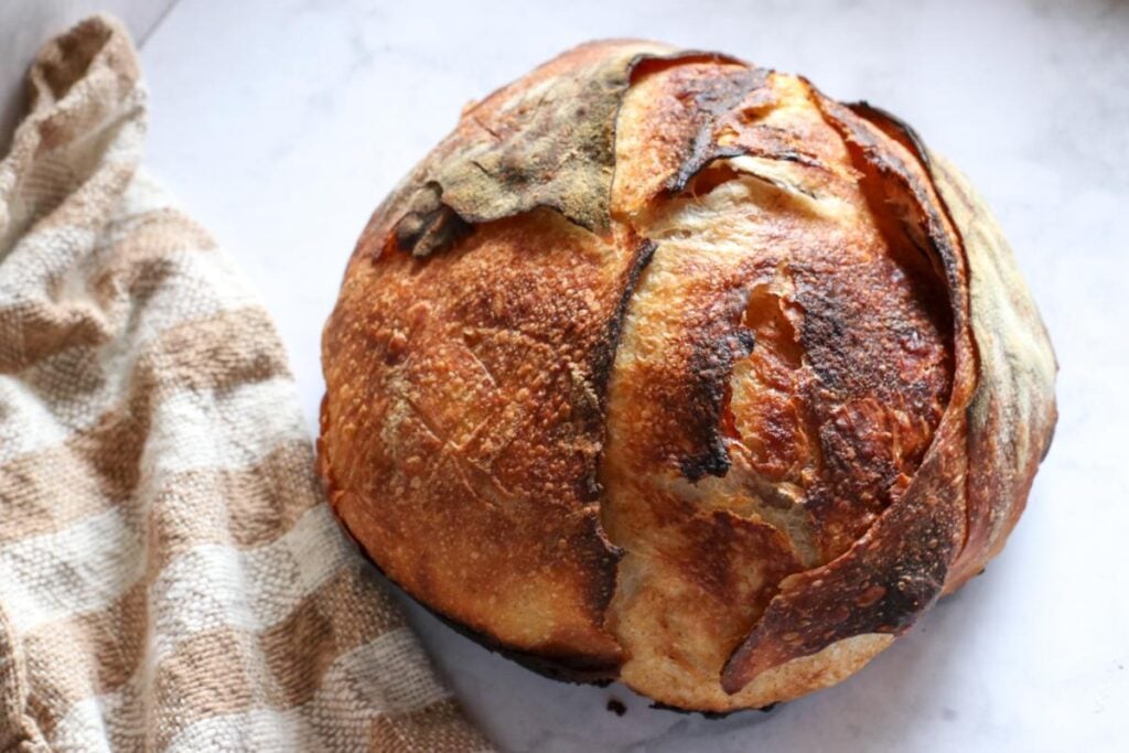 loaf of cinnamon honey butter sourdough bread on a marble counter with a brown and white checkered tea towel