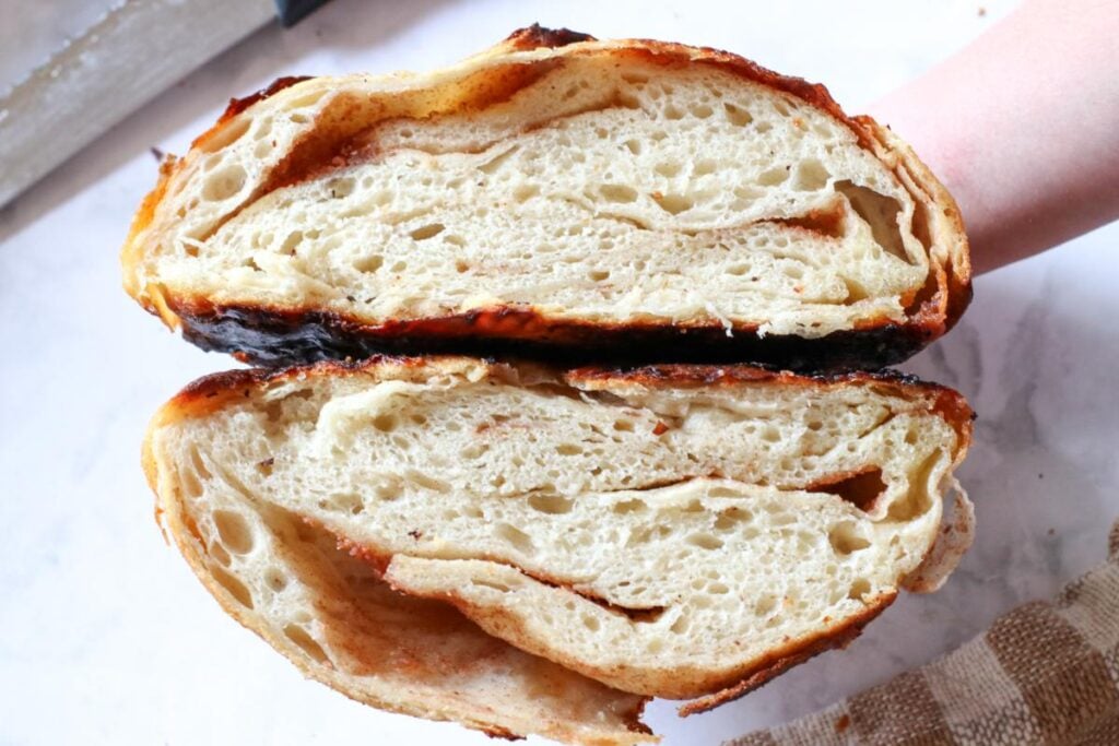 2 open halfs of cinnamon honey butter sourdough bread on a marble counter with a brown and white checkered tea towel