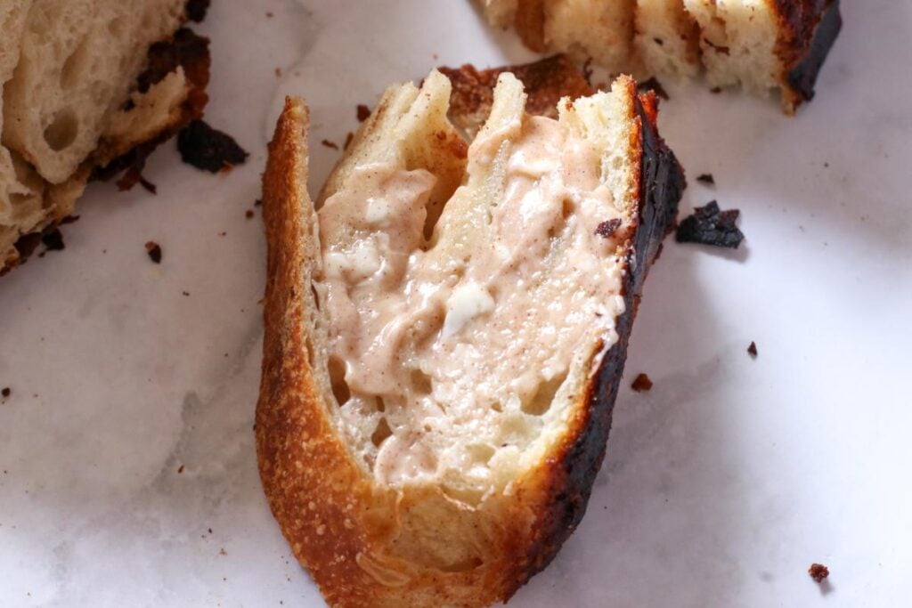 slice of cinnamon honey butter sourdough bread with more honey butter on top on a marble counter