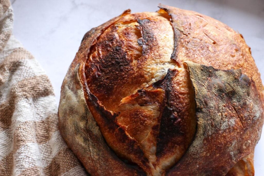 loaf of cinnamon honey butter sourdough bread on a marble counter with a brown and white checkered tea towel