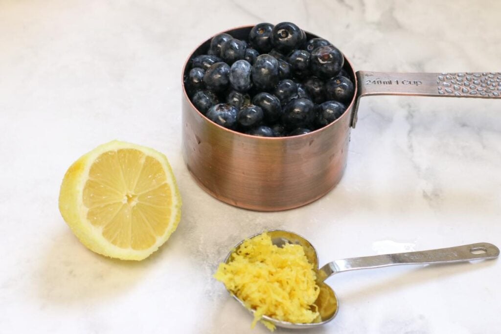 blueberries in a measuring cup, half a lemon and lemon zest in a measuring spoon