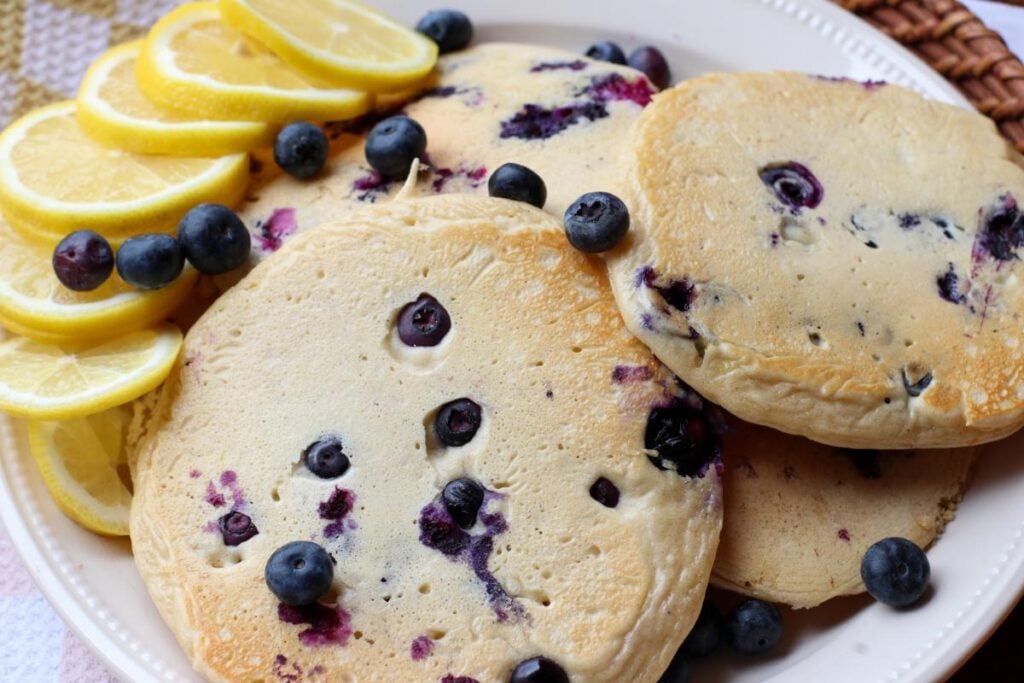 Lemon blueberry sourdough protein pancakes on a white plate with blueberries and slices of lemon