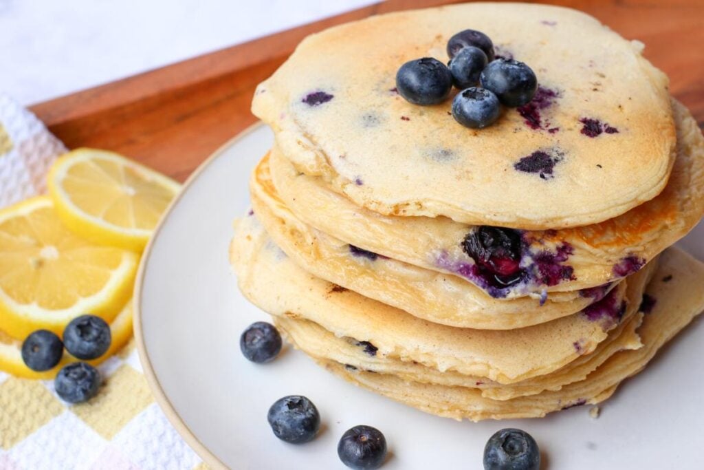 Lemon blueberry sourdough protein pancakes on a white plate with blueberries and slices of lemon