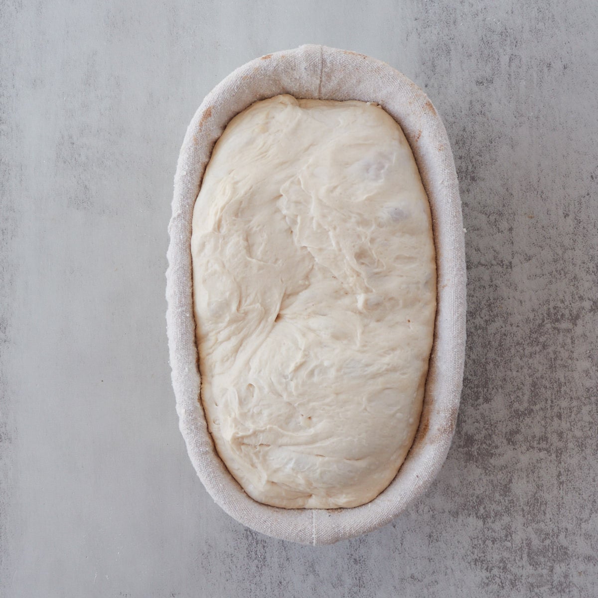 Sourdough bread dough in an oval banneton basket after second rise.