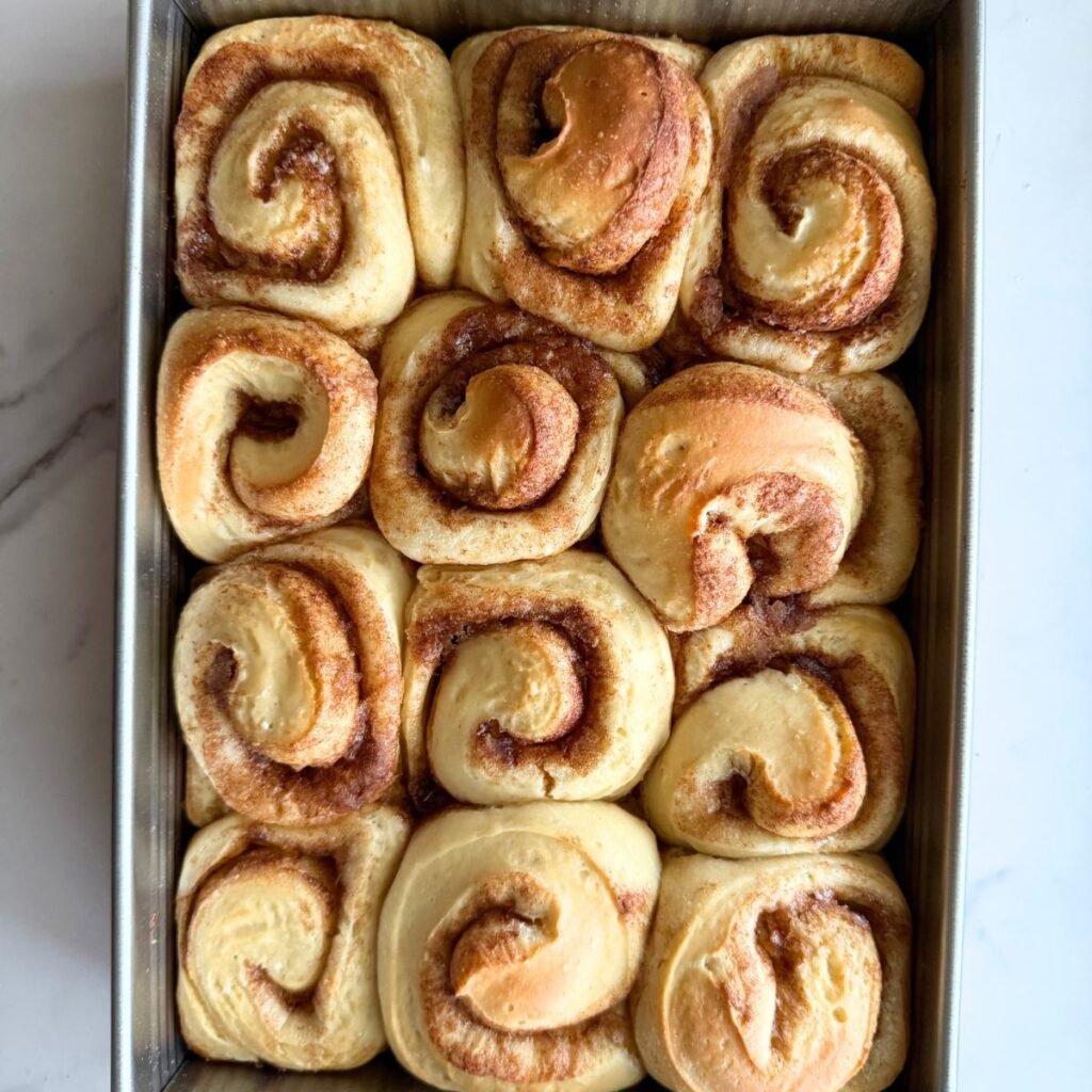 Freshly baked sourdough cinnamon rolls in a metal 9x13 pan.