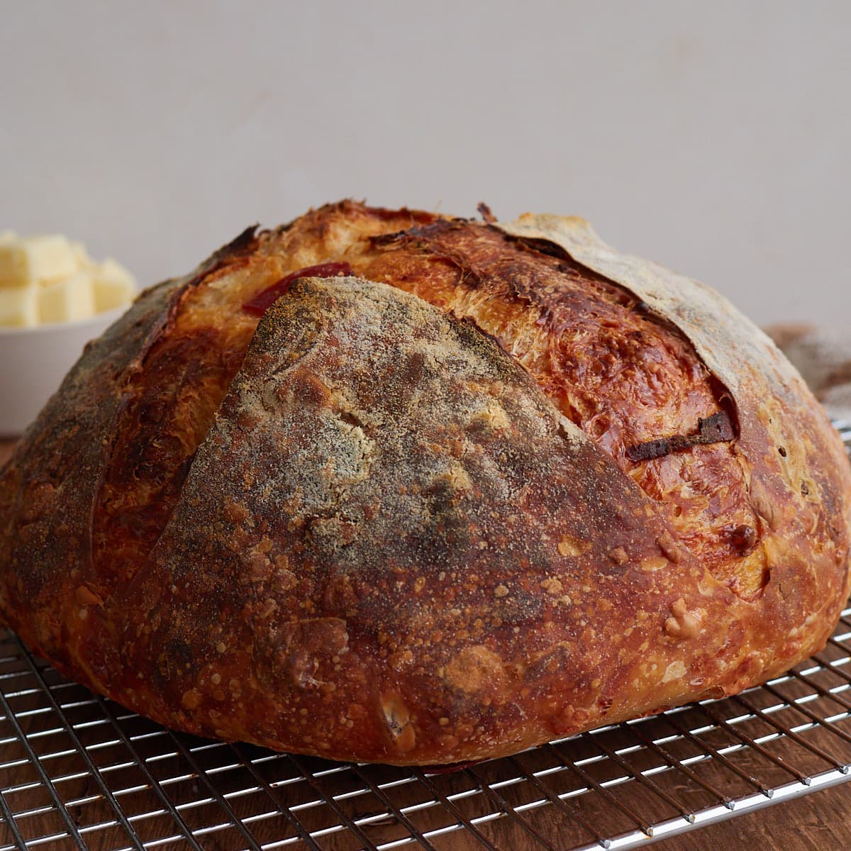 Loaf of pepperoni and cheese sourdough bread on a cooling rack with a pile of cubed cheese behind it. 