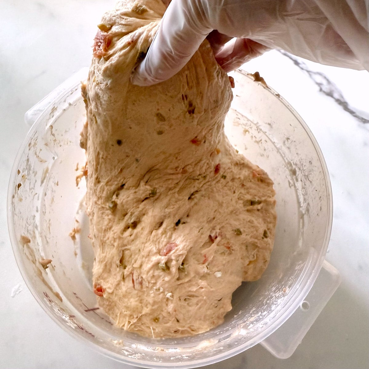 Stretching the sourdough salsa focaccia dough with one hand in a 2-quart clear bowl. 