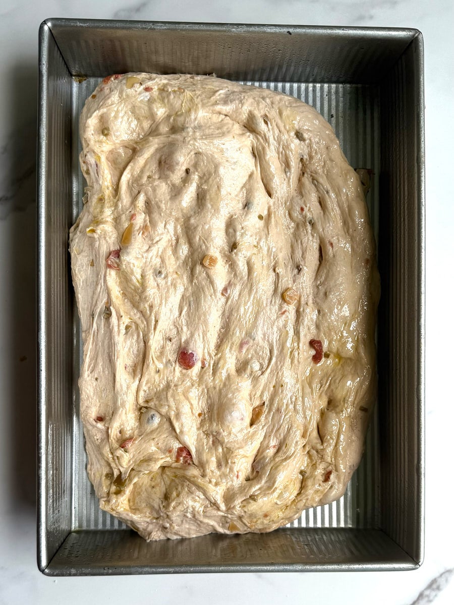 salsa focaccia dough stretched out in a 9x13 oiled pan before the final rise.