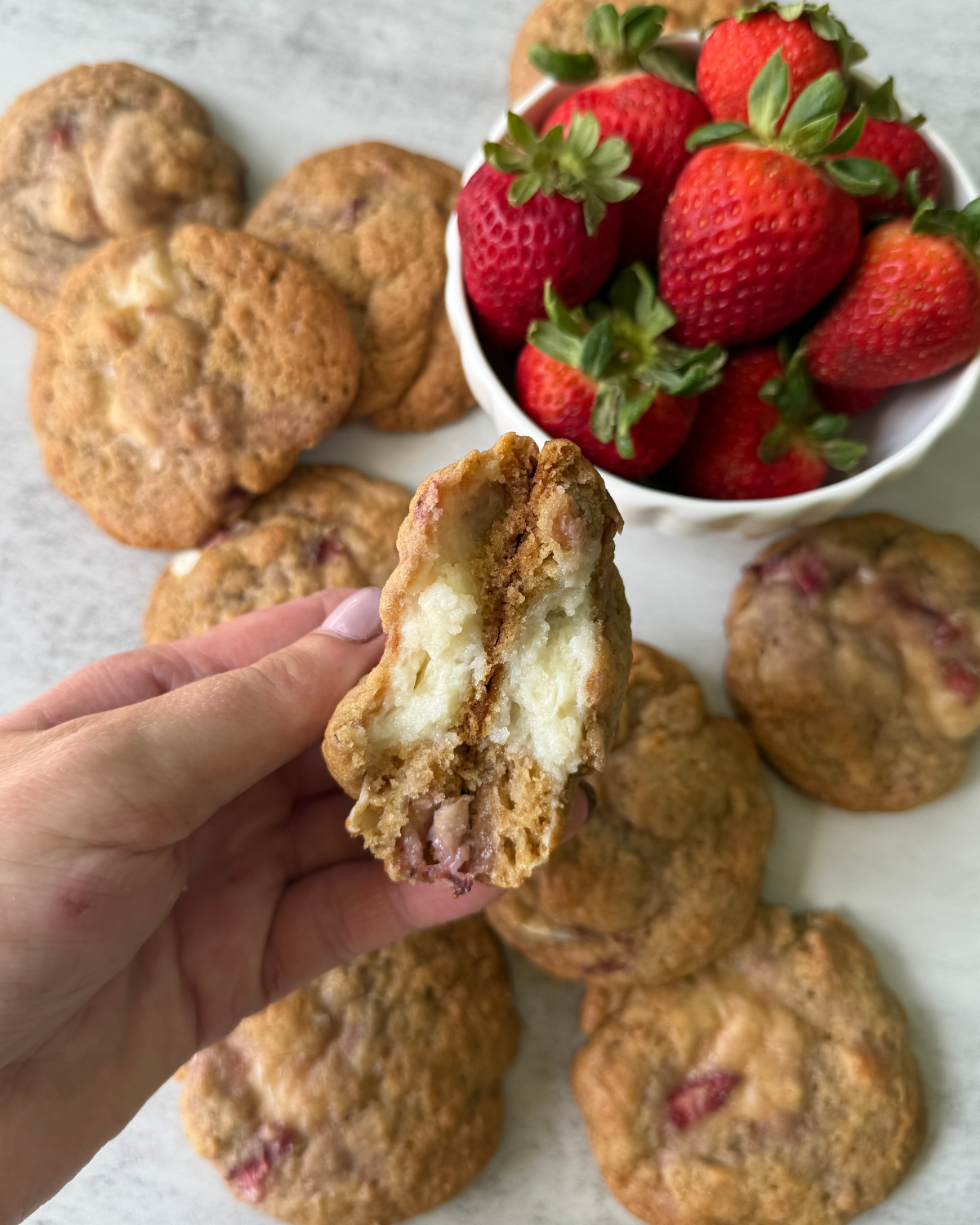 hand holding a strawberry cheesecake cookie with strawberries and more cookies in the background