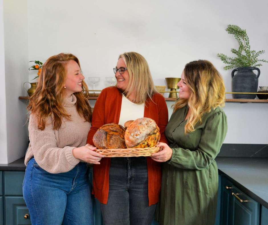 3 women in a kitchen holding a basket of bread