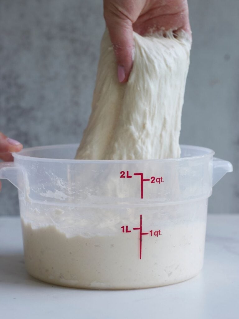 Hand pulling up sourdough focaccia dough to do a set of stretch and folds.