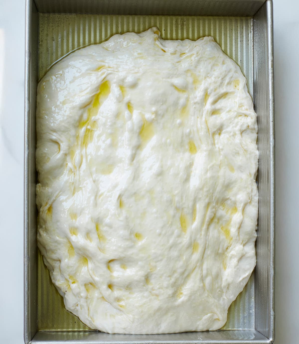 Sourdough cheeseburger focaccia dough in a greased metal 9x13 pan.