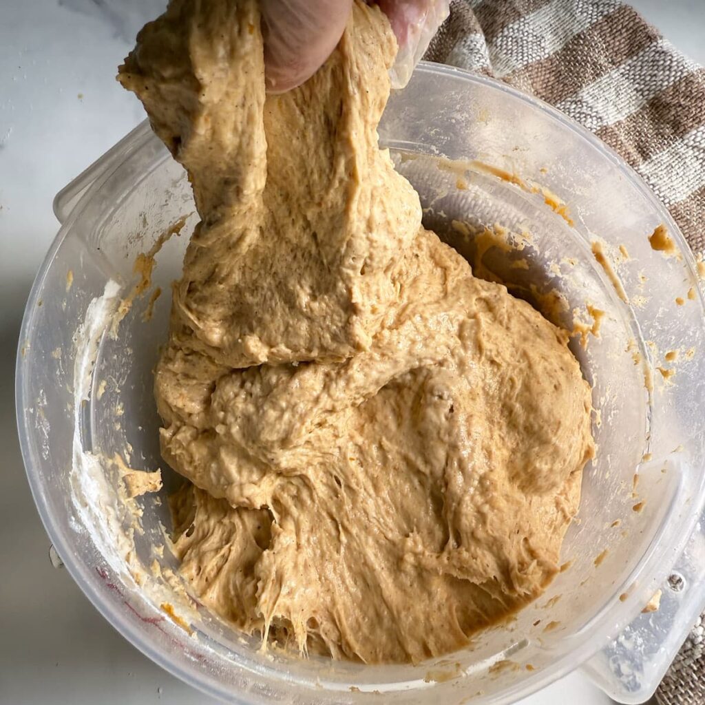A hand is stretching the sourdough pumpkin bread dough.