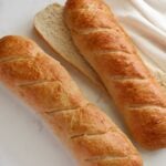 Two loaves of Sourdough Discard French Bread with one sliced down the center.