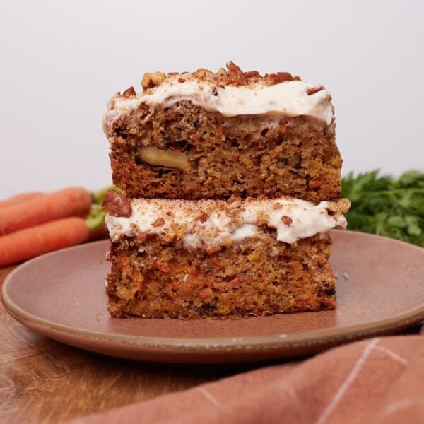 Two slices of Sourdough Carrot Cake stacked on top of each other on a brown plate.