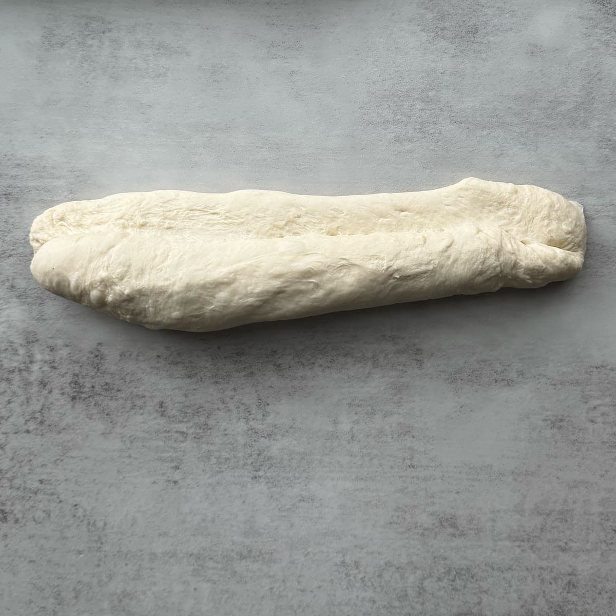 Sourdough discard french bread bring shaped into a long loaf on a marble surface.