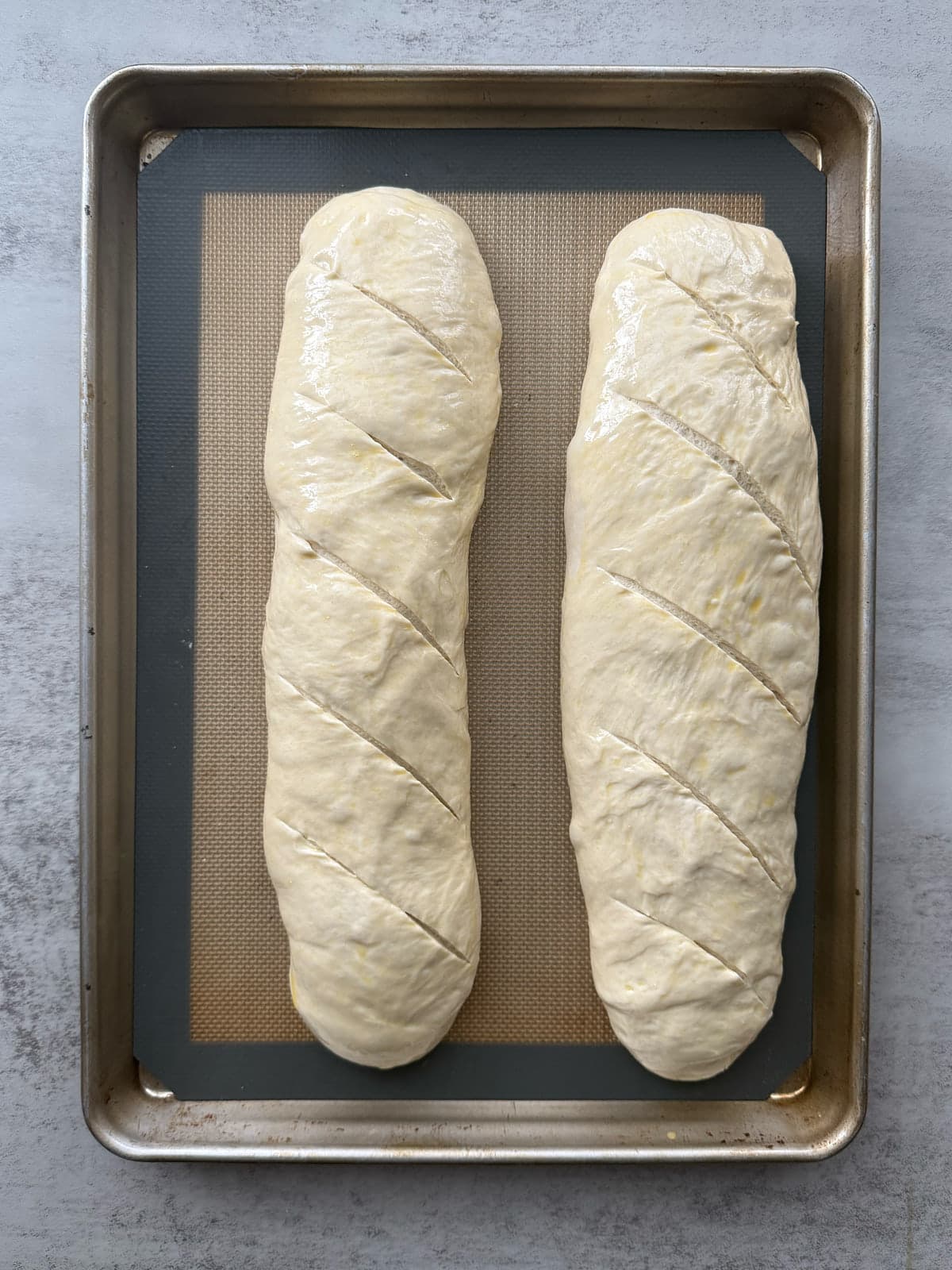 Two loaves of sourdough discard bread pre-bake arranged on a prepared baking sheet with an egg-wash.