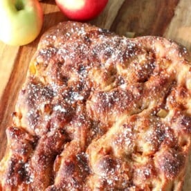 Caramel Apple Sourdough Focaccia on a wooden cutting board next to fresh apples.