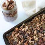 A mason jar filled with chocolate pumpkin sourdough granola next to a sheet pan filled with granola.