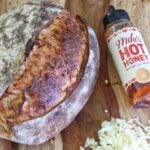 Hot Honey Parmesan Asiago Sourdough Bread loaf next to shredded cheese and a bottle of Mike's Hot Honey