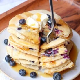 Stack of Lemon Blueberry Protein Sourdough Pancakes with fresh blueberries and a fork taking a slice.