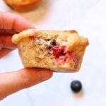 hand holding a Mixed Berry Sourdough Protein Muffins with a bite taken out.
