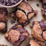 Oatmeal Chocolate Sourdough Cookie Bars on brown parchment paper next to a bowl of chocolate chips.