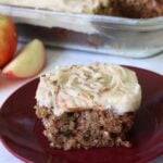 A slice of sourdough apple cake on top of a brown plate with cream cheese frosting.