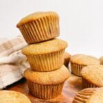 three Sourdough Banana Muffins stacked on top of each other next to a white and brown napkin.