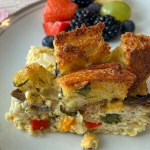 Slice of Sourdough breakfast casserole on a plate next to fresh fruit.