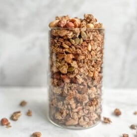 tall glass filled with sourdough granola on a white and gray background.