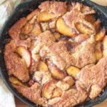 Sourdough peach cobbler in a cast iron skillet next to a white and brown napkin