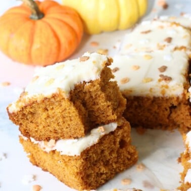 Slices of sourdough pumpkin cake stacked on top of each other next to small pumpkins.