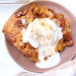 Sourdough pumpkin cobbler with pecans on a brown plate with a scoop of vanilla ice cream.