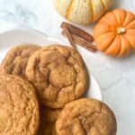 Sourdough Pumpkin Snickerdoodle cookies on a white plate next to cinnamon sticks and small pumpkins.