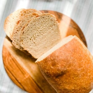 sliced sourdough sandwich bread on a round wooden cutting board.