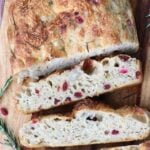 Slices of Stuffing Sourdough Focaccia next to fresh rosemary on a wooden cutting board.