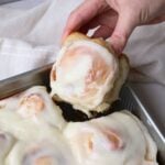 hand pulling out a sourdough cinnamon roll out of the pan