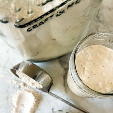 sourdough in a mason jar with some flour in a measuring cup spilling flour